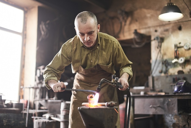 Il fabbro riscalda il bruciatore a gas il prodotto metallico sull'incudine