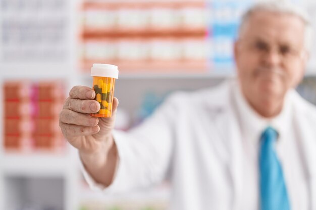 Il farmacista uomo dai capelli grigi di mezza età sorride fiducioso tenendo la bottiglia di pillole in farmacia