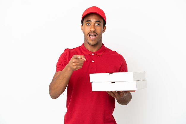 Il fattorino afroamericano della pizza che prende le scatole della pizza sopra la parete bianca isolata ha sorpreso e che indica front