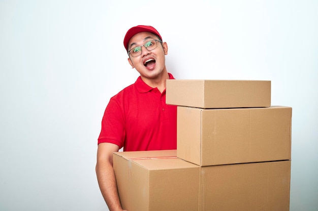 Il fattorino asiatico felice sorridente in uniforme di corriere rosso che guarda dietro le scatole con gli ordini dei clienti porta i pacchi a casa del cliente