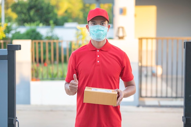 Il fattorino asiatico indossa una maschera protettiva in uniforme rossaConcetto di consegna di cibo e prodotti onlineNuova normalità in covid19