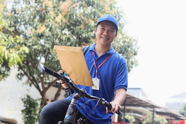 il fattorino che indossa l'uniforme blu porta la posta da inviare mentre si va in bicicletta.