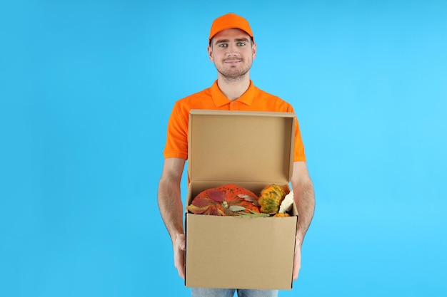 Il fattorino tiene la scatola con le zucche su fondo blu