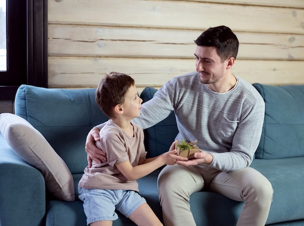 Il figlio fa un regalo a papà. Papà e figli su un divano blu in una casa in legno. I bambini augurano al padre un felice anno nuovo.