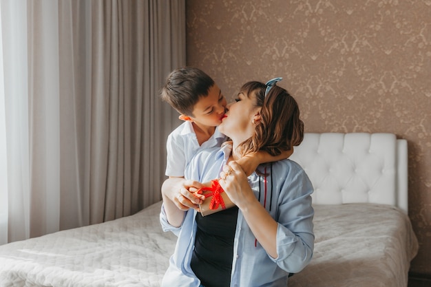 Il figlio fa un regalo alla mamma per la festa della mamma. mamma e bambino si siedono sul letto con una confezione regalo.