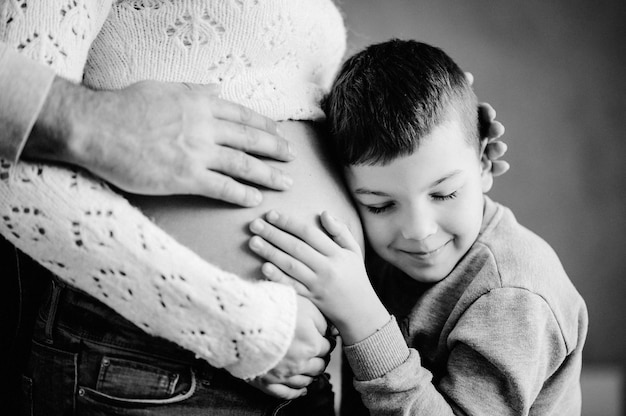 Il figlio sta ascoltando la pancia e sorridendo della sua bella madre incinta