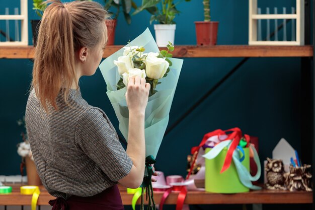 Il fiorista della giovane ragazza adulta fa un mazzo delle rose bianche.