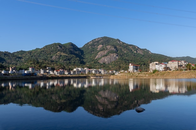 Il fiume di campagna riflette la montagna e i villaggi e le foreste sono sotto il cielo blu