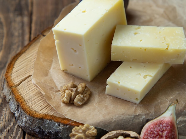 Il formaggio di fattoria di qualità giace su una tavola di legno circondato da fichi. uva e noci. primo piano su un vecchio tavolo di legno