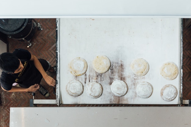 Il fornaio artigianale insegna al suo apprendista di affettare la pasta per pane lievitato prima di cuocere in forno elettrico