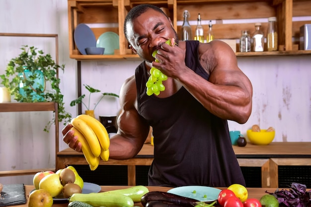 Il forte uomo di colore morde l'uva in cucina