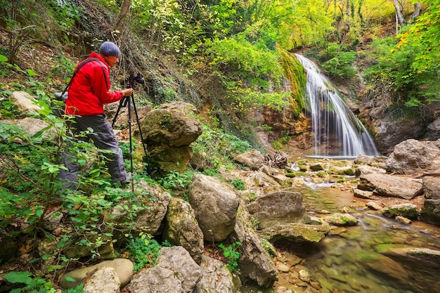 Il fotografo che fotografa il paesaggio di montagna con una cascata in autunno