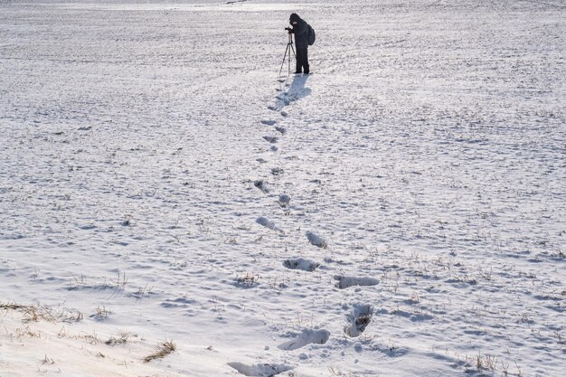 Il fotografo con un treppiede in un campo innevato scatta foto di impronte di paesaggi invernali nella neve