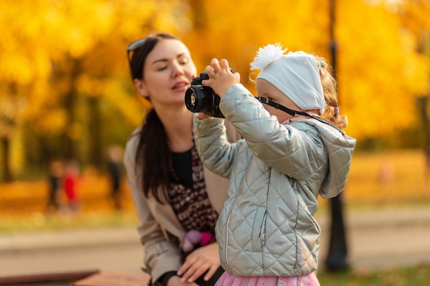 Il fotografo di una bambina con una macchina fotografica fa una foto nel parco giallo autunnale. Figlia con mamma in natura