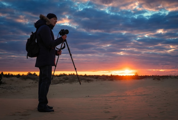 Il fotografo riprende paesaggi durante il tramonto sulla sabbia. Bellissimo cielo colorato all'alba. Creatività e successo.