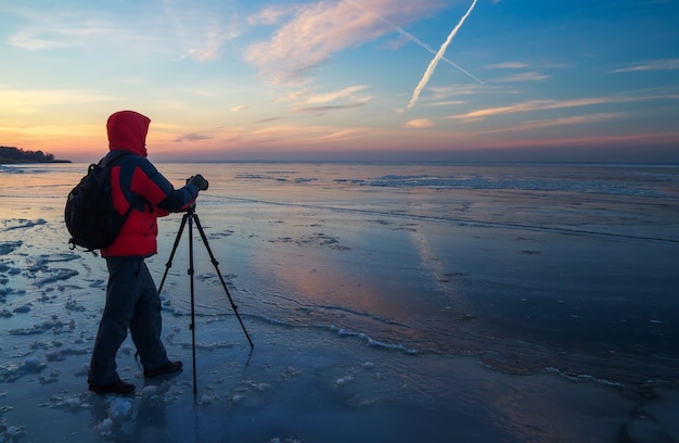 Il fotografo scatta foto sul fiume ghiacciato durante il tramonto