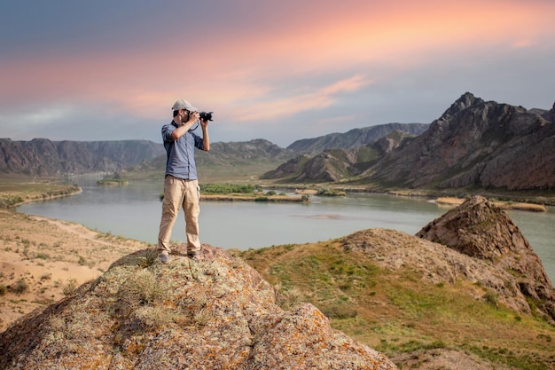 Il fotografo scatta un paesaggio dalla cima di una montagna sulle rive del fiume al tramonto