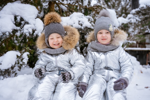 Il fratellino e la sorella in inverno camminano nel parco in tuta invernale siedono nella neve sullo sfondo o...