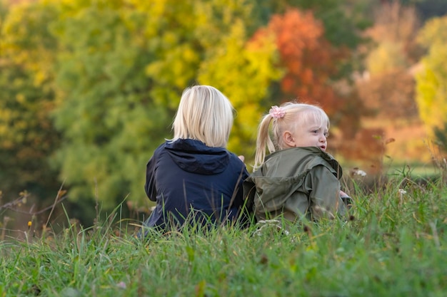 Il fratellino e la sorella si siedono sull'erba sullo sfondo degli alberi autunnali I bambini biondi camminano nella natura il giorno dell'autunno