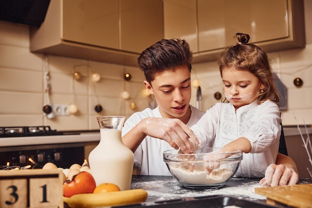 Il fratello con la sua sorellina prepara il cibo usando la farina in cucina e divertiti.