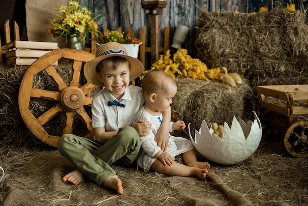 Il fratello e la sorella caucasici felici in vestiti di lino si siedono sulla superficie del fieno nella zona di Pasqua. Vacanze di Pasqua per i bambini