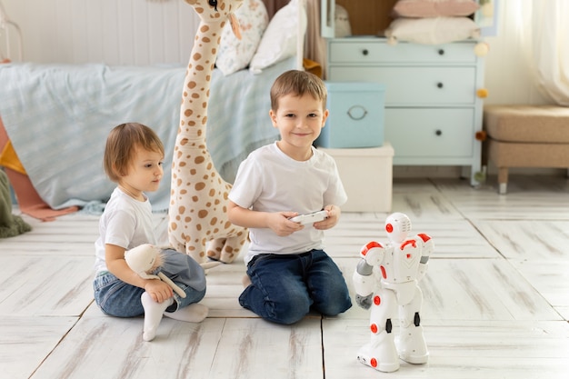 Il fratello e la sorella dei bambini piccoli si siedono per terra nella stanza, ridono e giocano con il robot