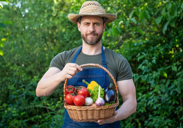 Il fruttivendolo in cappello di paglia tiene il cesto pieno di verdure