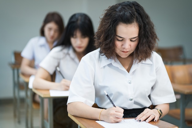 Il fuoco selettivo degli studenti universitari adolescenti si siedono sulla sedia della lezione, scrivono sul foglio di risposta della carta d'esame prendendo la stanza dell'esame finale o l'aula. Studenti universitari in uniforme in aula.