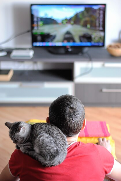 Il gatto si siede sulla spalla di un uomo con una grande TV dietro di lui