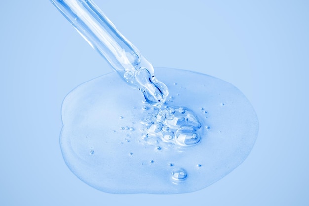Il gel cosmetico trasparente scorre da un contagocce direttamente sullo sfondo in una grande macchia con bolle Su uno sfondo blu Crema gel toner toner all'acido ialuronico Cosmetici