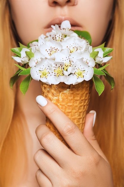 Il gelato a base di fiori in un cono di cialda è tenuto da una giovane donna a livello delle labbra per mangiare