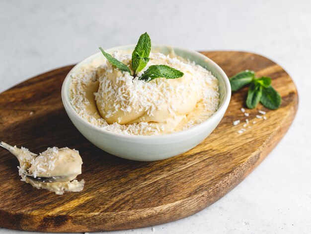 Il gelato vegano fatto in casa in una ciotola è fatto con mango congelato e latte di cocco servito da menta fresca e scaglie su una tavola di legno strutturata