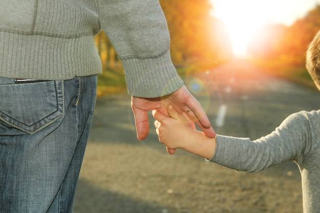 Il genitore tiene la mano di un bambino che cammina vicino a una strada