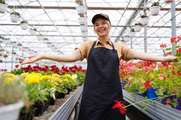 Il giardiniere femminile in una serra di fiori saluta con le braccia tese