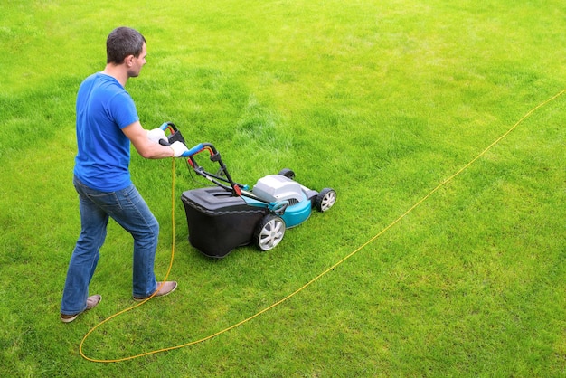 Il giardiniere nel giardino falcia l'erba con un tosaerba Vista laterale