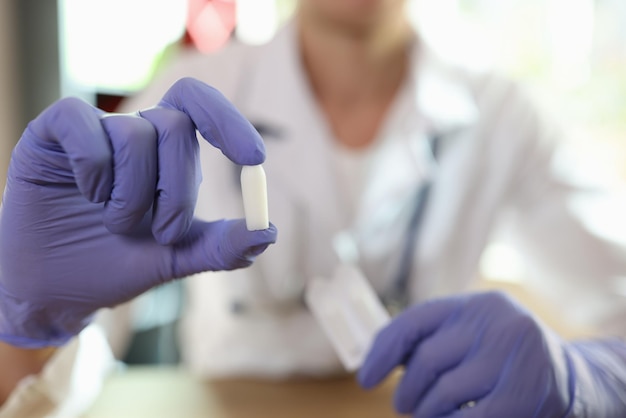 Il ginecologo in guanto mostra le supposte in mano mentre è seduto nell'ufficio della clinica medica