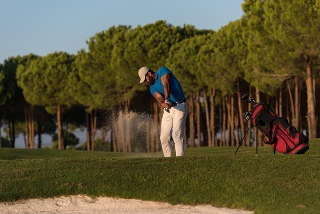 il giocatore di golf ha sparato palla dal bunker di sabbia al campo da golf con un bel tramonto sullo sfondo