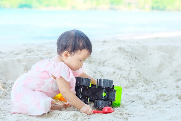 Il gioco della bambina del primo piano con la sabbia ed il giocattolo su spiaggia hanno strutturato il fondo con lo spazio della copia