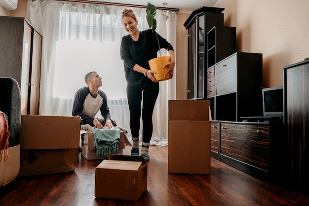 Il giorno del trasloco si trasferisce nella nuova casa giovane coppia felice famiglia di sposini che si diverte in camera con la pianta d'appartamento