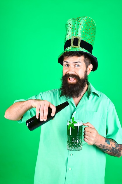 Il giorno di san patrizio uomo barbuto felice con cappello da leprechaun versa birra in vetro ritratto di uomo felice