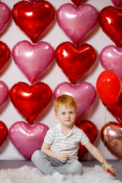 Il giorno di San Valentino, il 14 febbraio, un ragazzo dai capelli rossi siede tra le palle con i cuori Amore in tutto il mondo