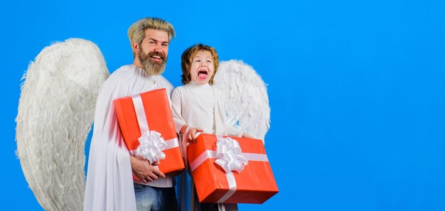 Il giorno di San Valentino piccolo ragazzo cupido e uomo barbuto in ali d'angelo con regalo di San Valentino padre e figlio