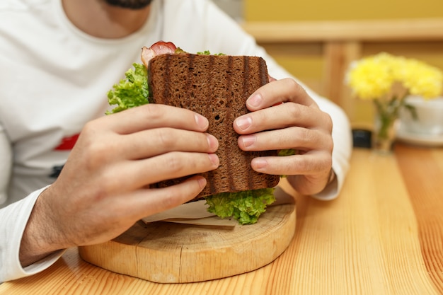 Il giovane affamato in resaurant mangia il panino