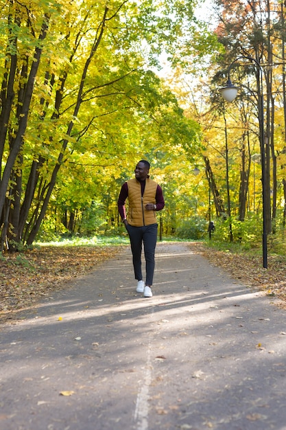 Il giovane afroamericano allegro in vestiti alla moda cammina nel parco di autunno il giorno soleggiato caldo di autunno