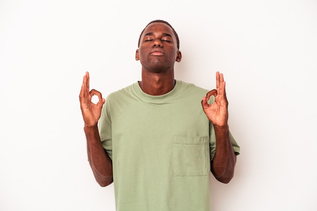 Il giovane afroamericano isolato su sfondo bianco si rilassa dopo una dura giornata di lavoro, sta eseguendo lo yoga.