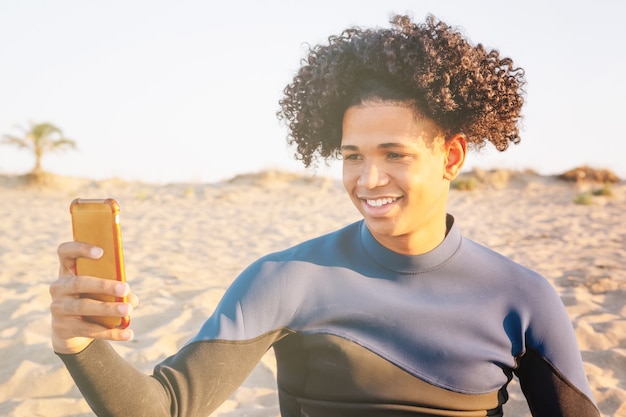 Il giovane afroamericano seduto sulla sabbia scatta una foto con uno smartphone