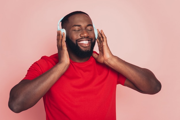 Il giovane afroamericano si gode la musica con le cuffie su sfondo rosa