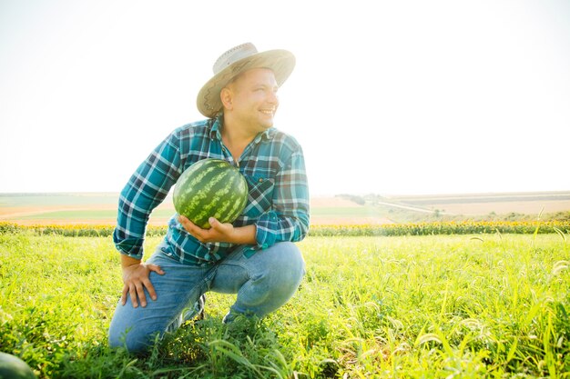 Il giovane agricoltore con il cappello è nel campo delle angurie contro lo sfondo del cielo