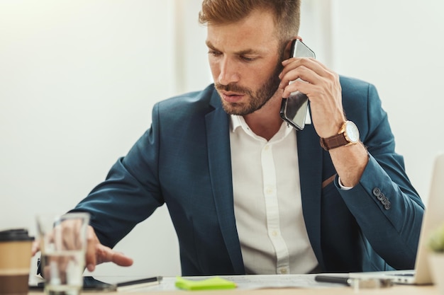 Il giovane architetto di successo sta parlando su smartphone e utilizzando tablet digitale mentre lavora ai progetti di un nuovo progetto in ufficio.