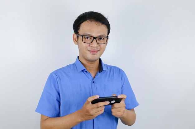 Il giovane asiatico si diverte e sorride sullo smartphone quando gioca Uomo indonesiano che indossa una camicia blu